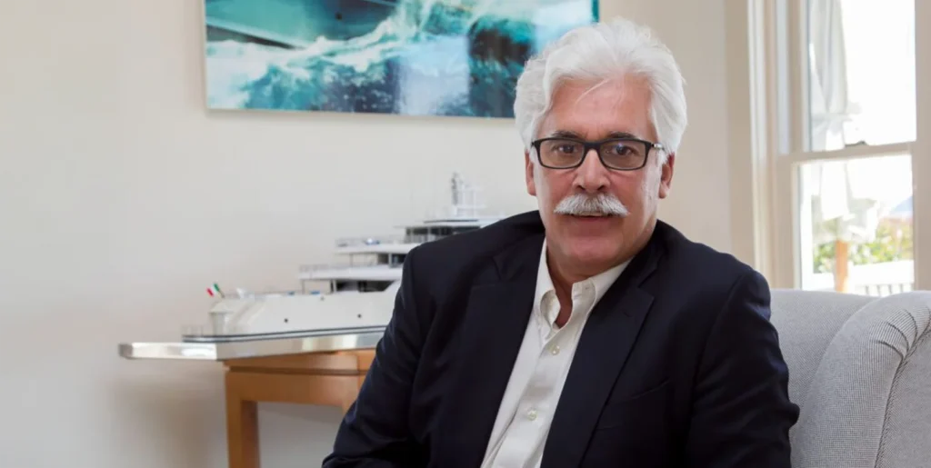Bruce Brakenhoff Jr. sits for a portrait with a model yacht in the background.